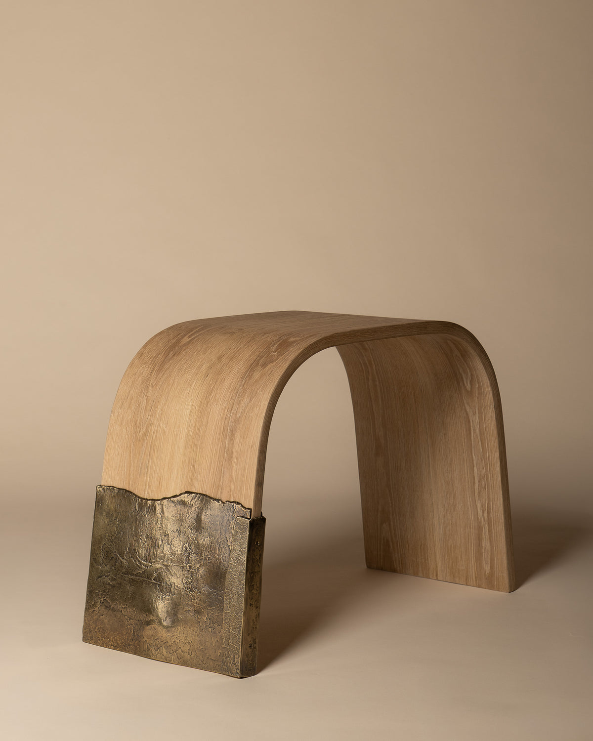 Brume oak bench with a sculptural brass leg, three-quarter view.