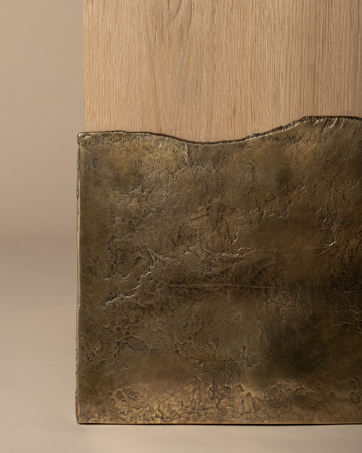 Close-up of Brume's textured brass leg and irregular edge against the oak.
