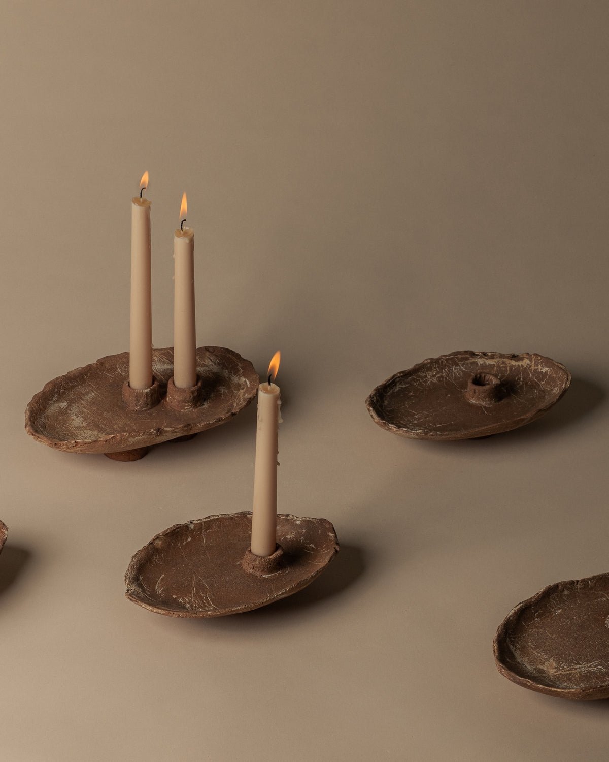 Utah Clay single candlesticks with different handmade forms and surface markings, shown with a double candlestick and lit candles. Sold individually.