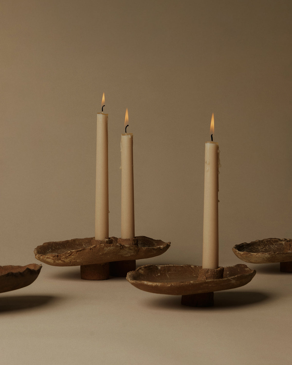 Utah Clay double candlestick holding two lit candles, shown beside single candlesticks to reveal their handmade rims, texture and raised feet. Sold individually.
